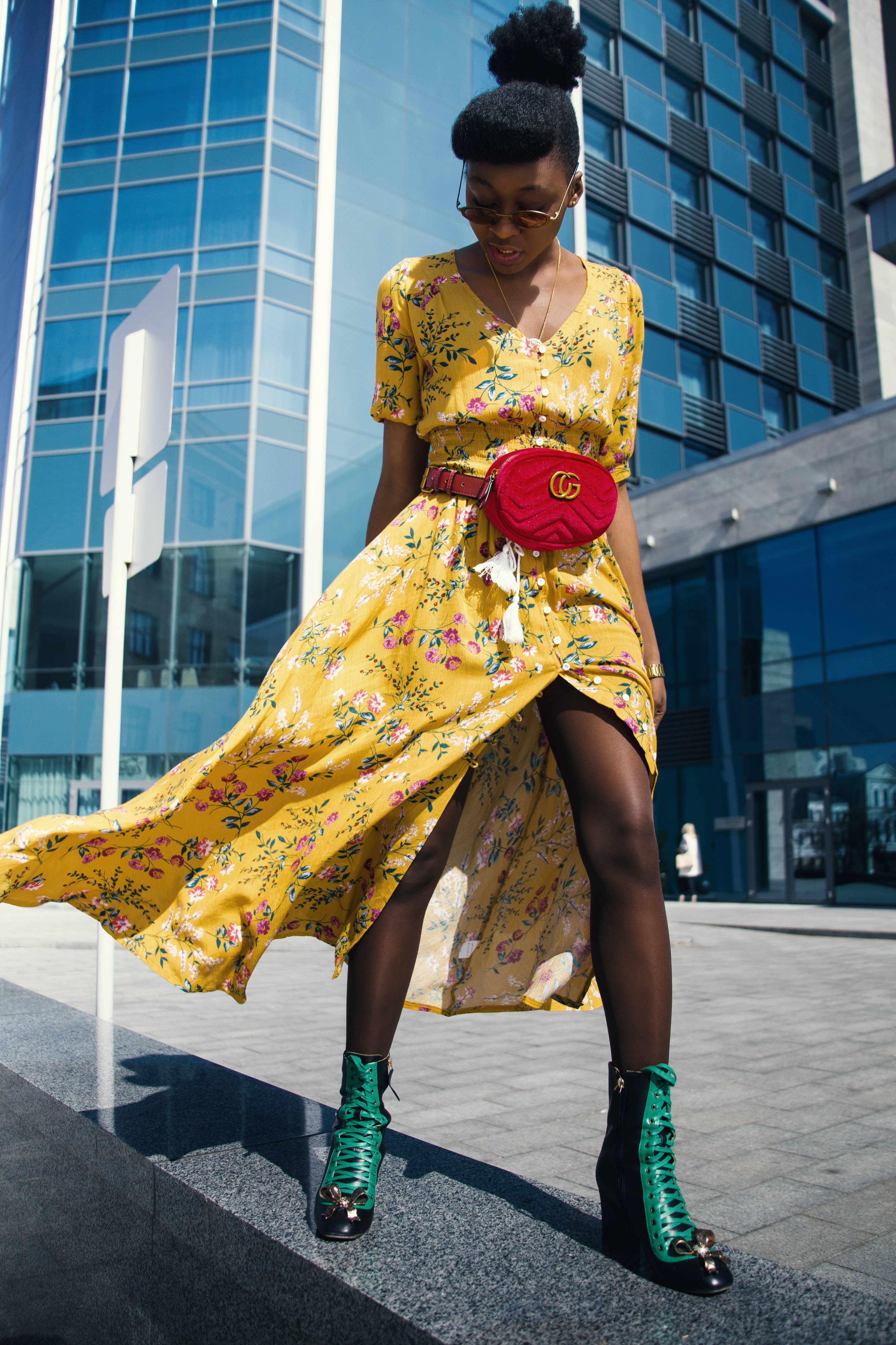 Image of a woman sitting down wearing a long yellow dress with various flowers on it.